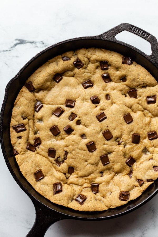 top down shot of black cast iron skillet with a skillet cookie in covered in chocolate chunks. On a marble background 