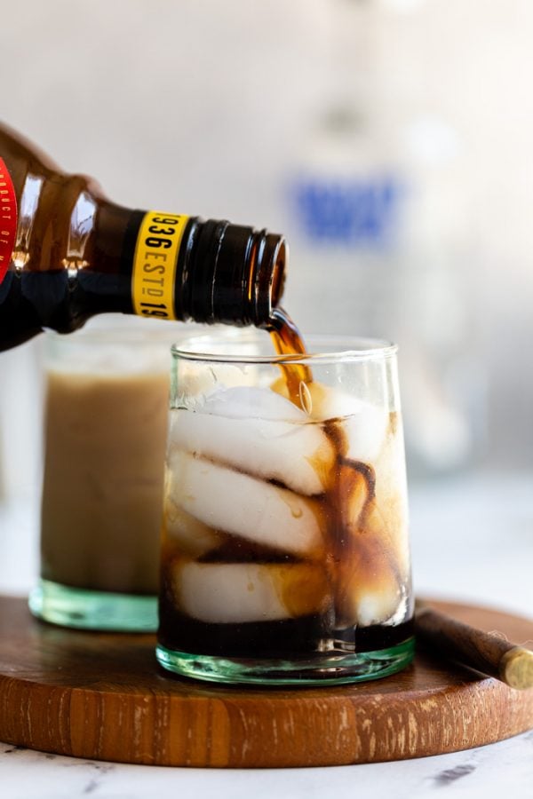 small cup of a white russian: black liquid on ice with kahlua being poured into the glass