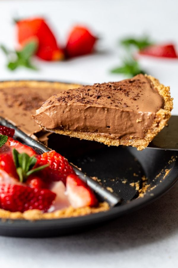 double sided "split decision pie" with a chocolate silken pie on one side and a fresh strawberry pie on the other. Fresh strawberries and mint are around the edges of the frame. This image shows an up close shot of a piece of chocolate pie coming out of the dish