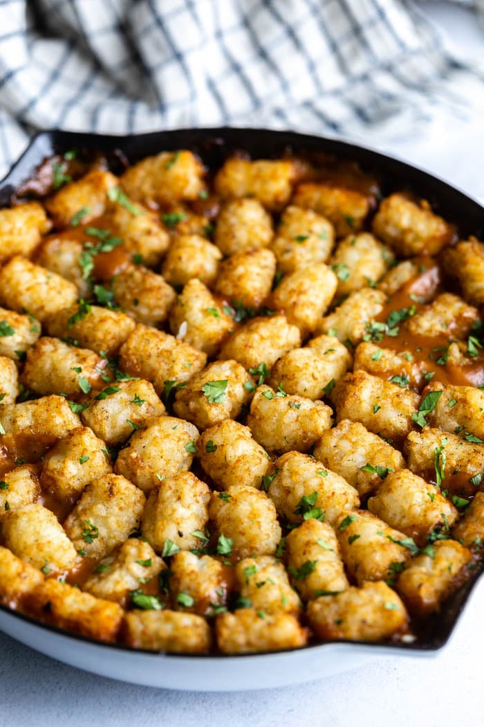 white skillet filled with tater tot casserole with the tater tots on the top in a circular pattern