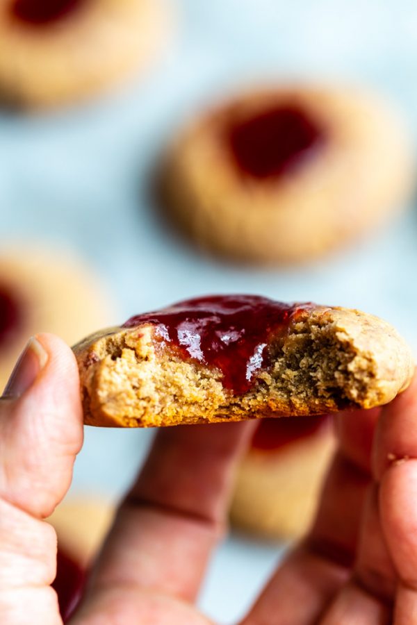 peanut butter thumbprint cookies with a dollop of strawberry jam on top. Up close shot of one cookie being held with several cookies in the background