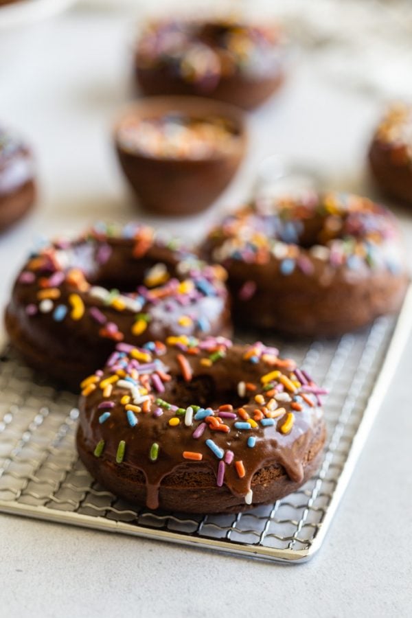 chocolate glazed donuts topped with sprinkles and sprinkles all around the shot. the donuts are sitting on top of a cooling wrack