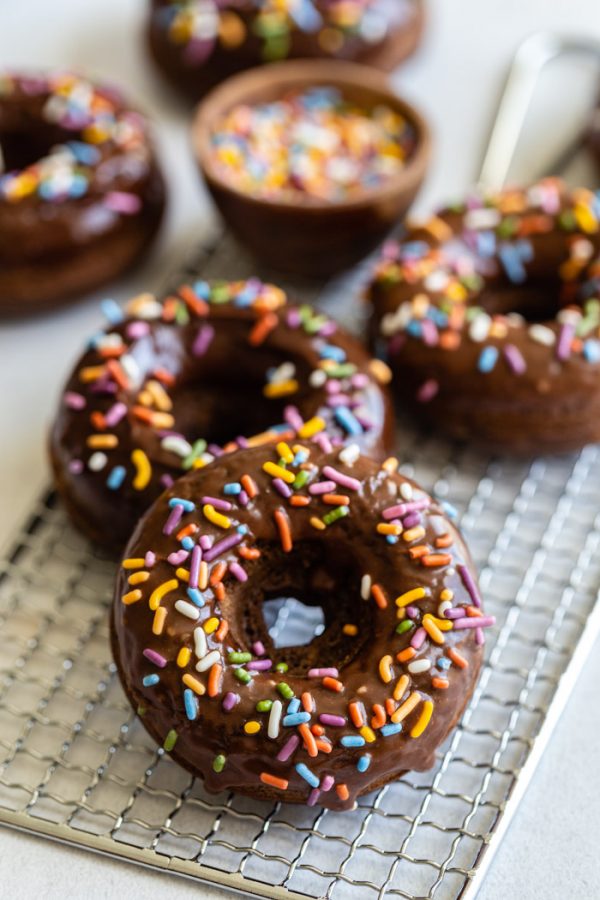 chocolate glazed donuts topped with sprinkles and sprinkles all around the shot. the donuts are sitting on top of a cooling wrack