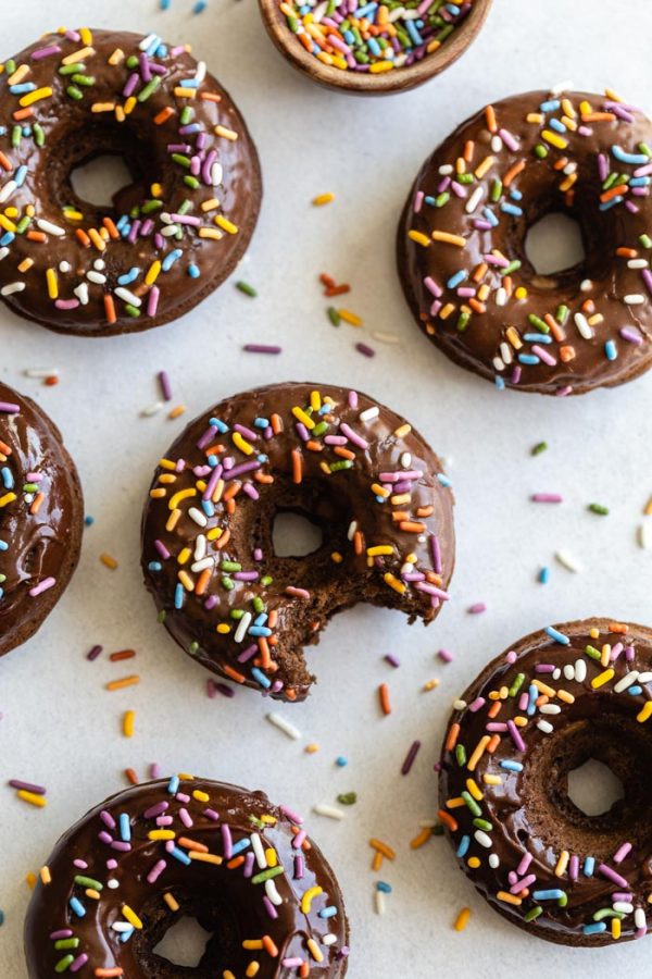 chocolate glazed donuts topped with sprinkles and sprinkles all around the shot. The center donut in the shot has a bite taken out