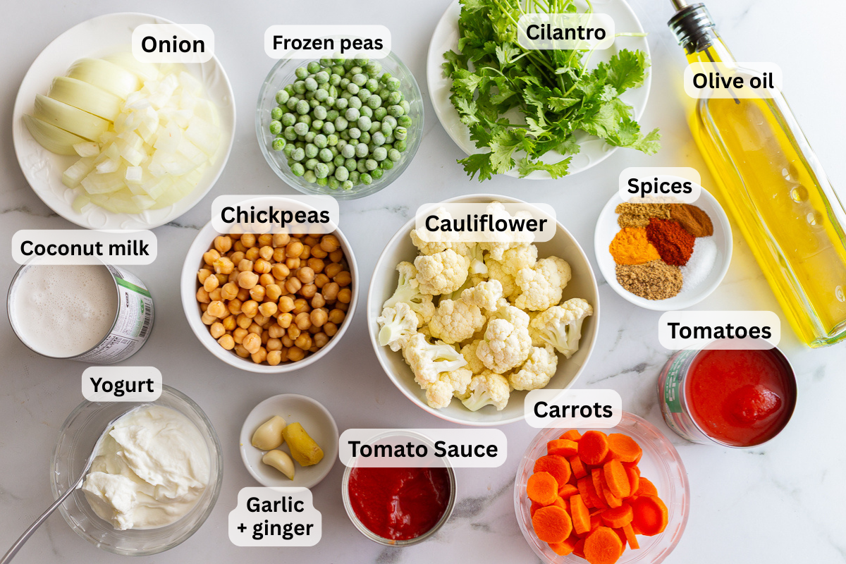 labeled ingredients need to make a vegetarian tikka masala including chickpeas, oil, spices, onion, carrot, cauliflower, coconut milk, tomato sauce, canned tomatoes, ginger and garlic