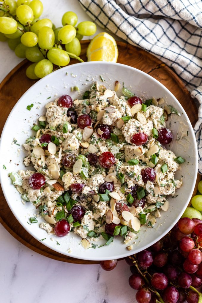 white bowl filled with "vegan chicken salad" that has chunks of tofu, veggies and grapes in it"vegan chicken salad" that has chunks of tofu, veggies and grapes in it