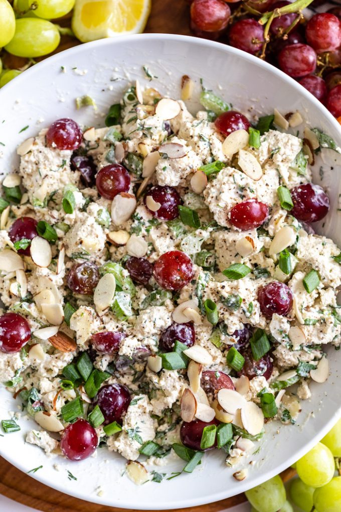 hvit bolle fylt med "vegansk kyllingsalat" som har biter av tofu, grønnsaker og druer i den"vegan chicken salad" that has chunks of tofu, veggies and grapes in it