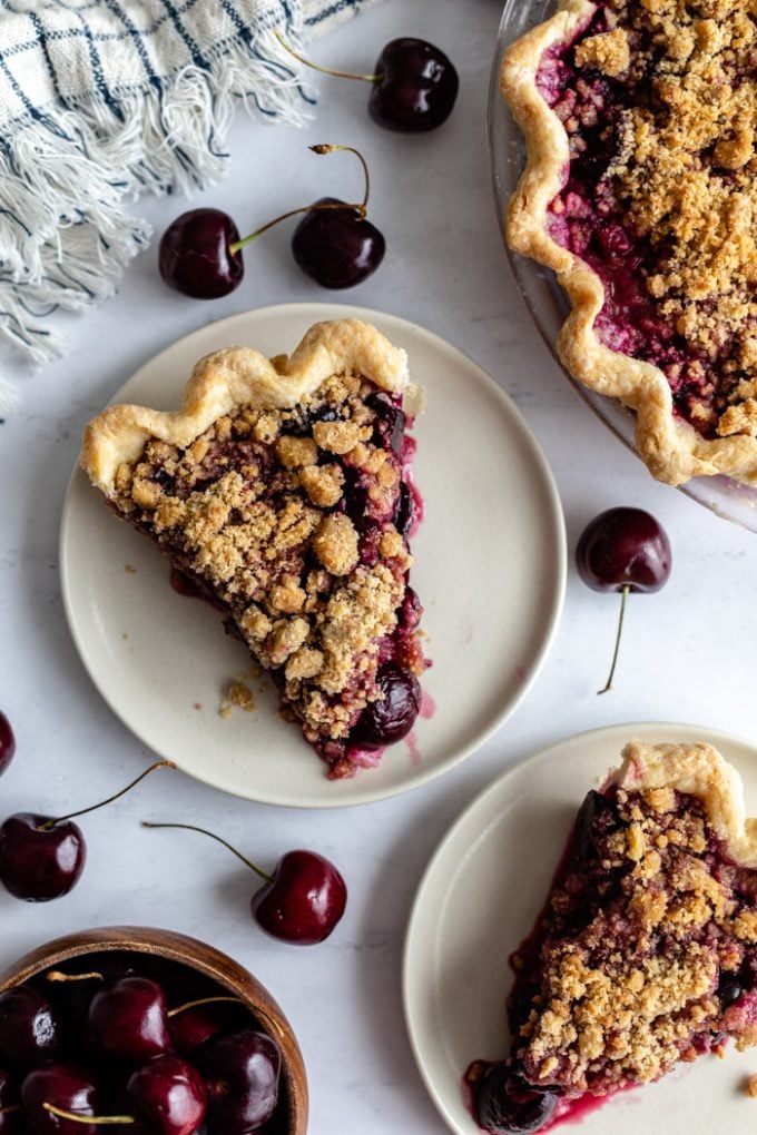 top down shot of slices of cherry pie with crumble topping. fresh cherries around the scene