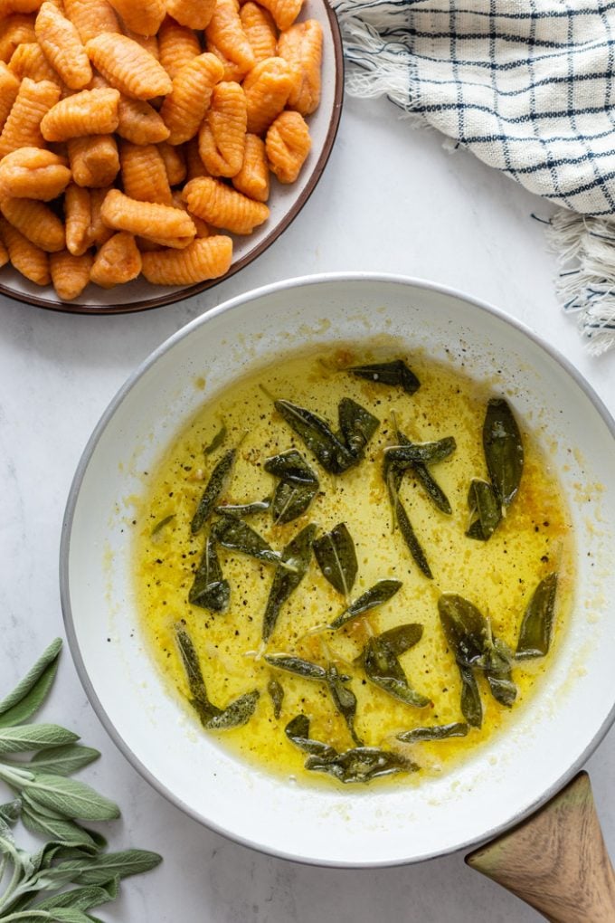 sage butter sauce in a white skillet with sweet potato gnocchi in a bowl next to it