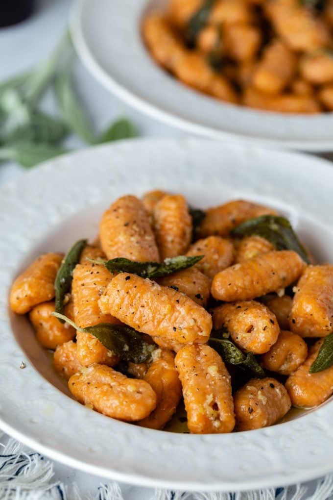 side shot of sweet potato gnocchi in a sage sauce. In a white bowl with another bowl in the background