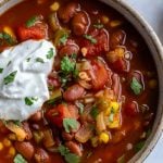 up close shot of instant pot vegetarian chill topped with fresh herbs and sour cream with chips in the background