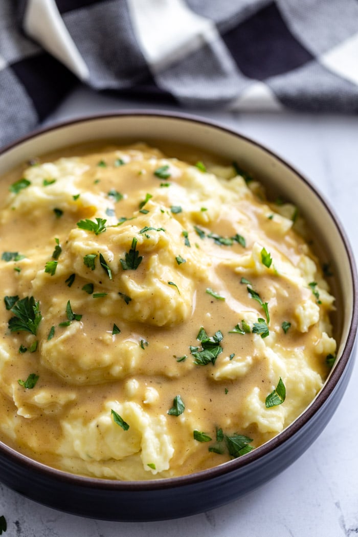big bowl of mashed potatoes covered with a brown vegan gravy sauce and sprinkled with fresh herbs