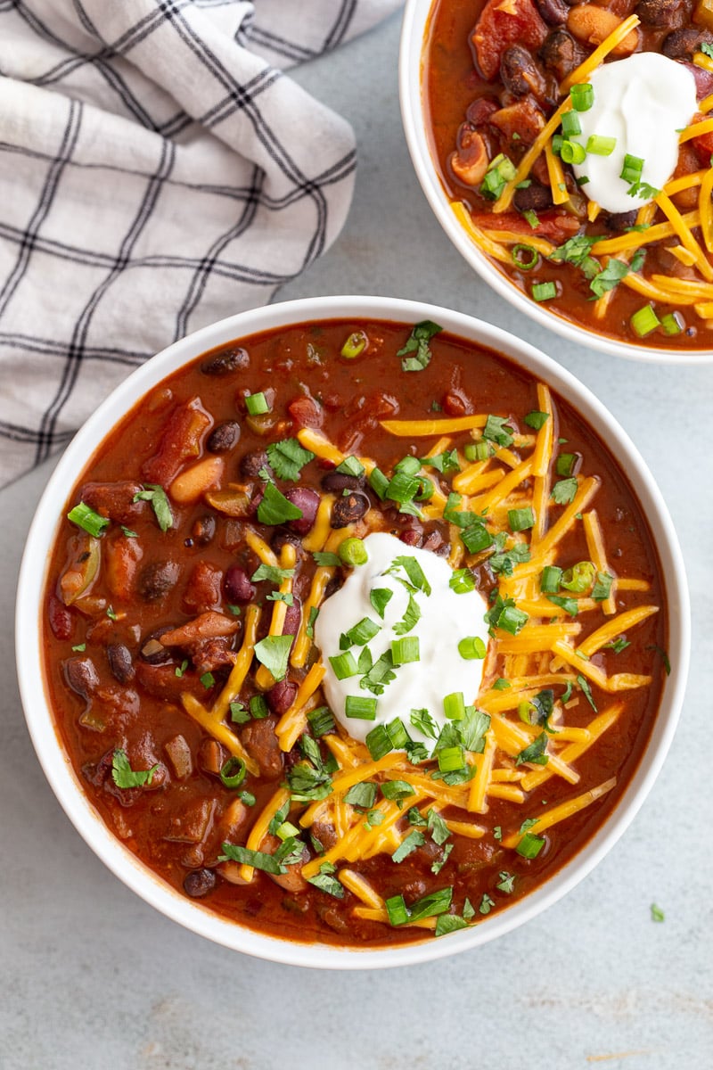 Chili made with beans served in a white bowl with sour cream, cheese and green onion.