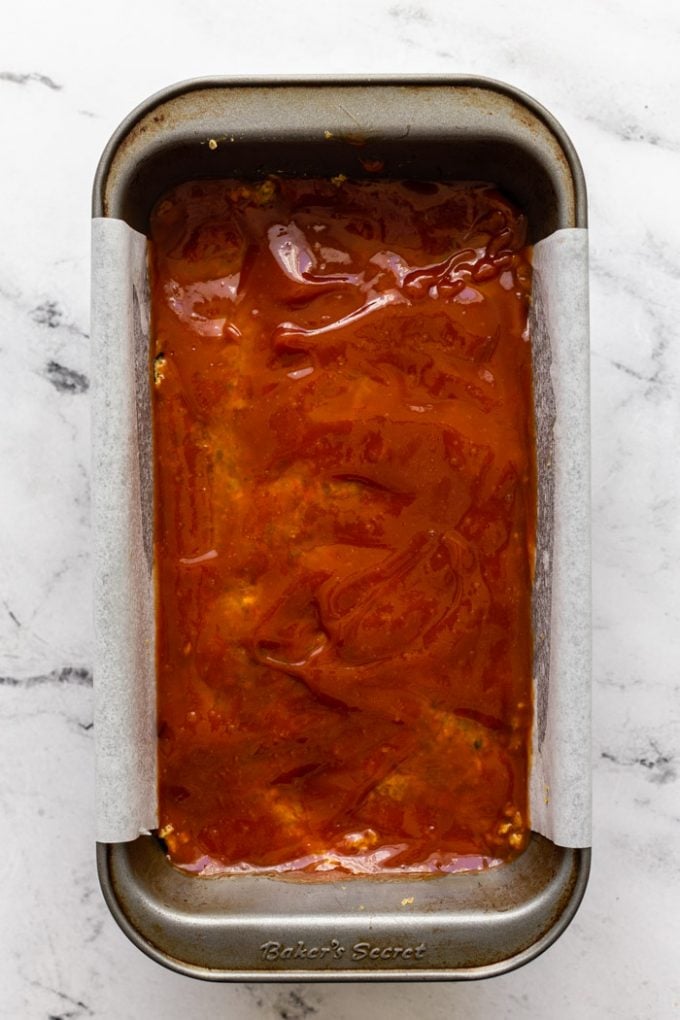 top down shot of vegan meatloaf in a loaf pan lined with parchment paper. on a marble board