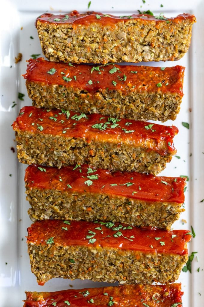 lentil meatloaf topped with ketchup and parsley. Sliced on a white plate