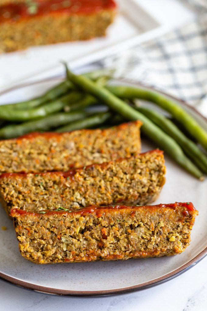 lentil meatloaf topped with ketchup and parsley. Sliced on a plate with green beans