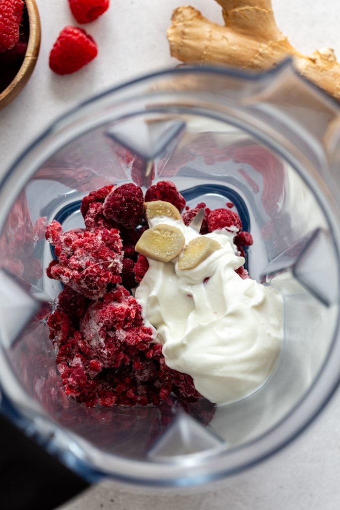 inside of a blender that's filled with frozen raspberries, yogurt, ginger