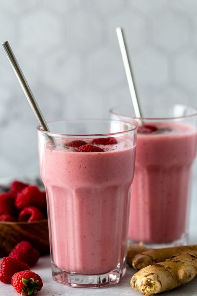 2 pink raspberry smoothies with fresh raspberries and chia seeds on top