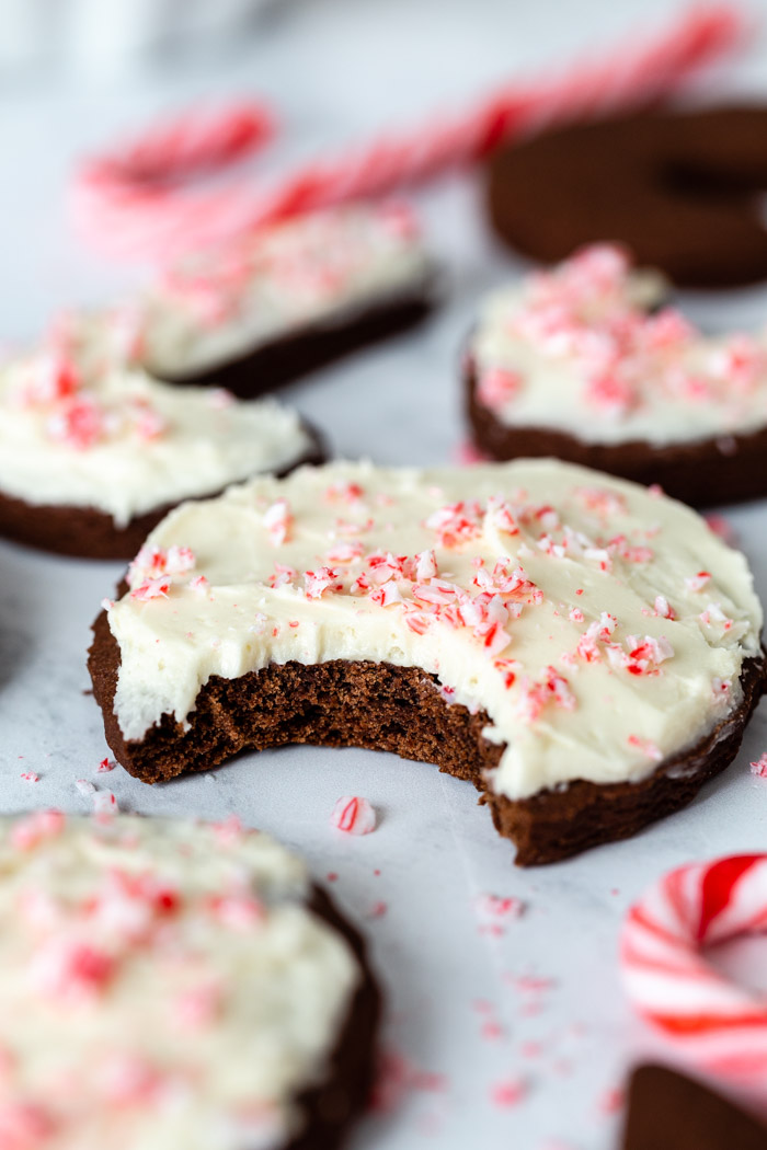 up close shot of a round chocolate sugar cookie that's topped with vanilla frosting and crushed peppermint. more cookies in the background