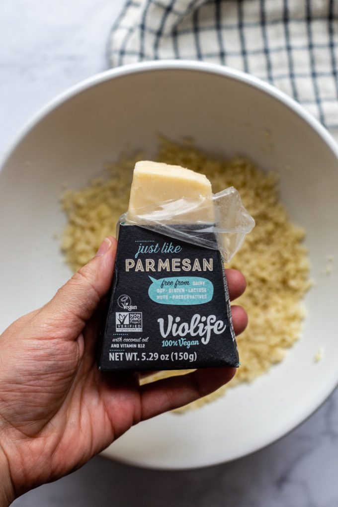 blok af violife vegan parmesanost holdes over en skål brødkrummer