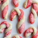 red and white sugar cookies that are twisted to look like candy canes. All laying on parchment paper