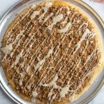 large cinnamon sugar dessert pizza on a pizza pan and drizzled with frosting
