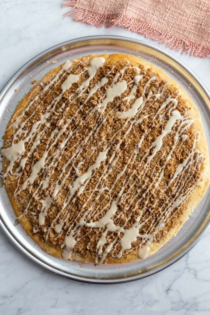 large cinnamon sugar dessert pizza on a pizza pan and drizzled with frosting