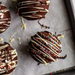hot chocolate bombs topped with drizzled chocolate and sprinkles/ crushed peppermint all sitting on a baking sheet