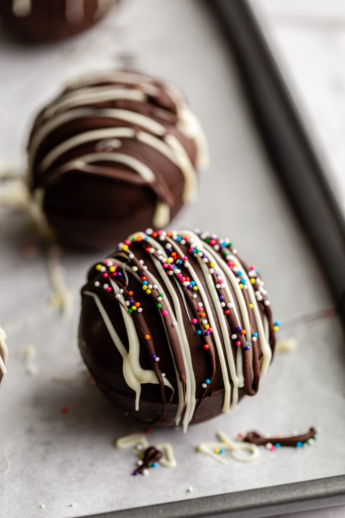 hot chocolate bombs topped with drizzled chocolate and sprinkles/ crushed peppermint all sitting on a baking sheet