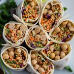 tortilla wraps filled with coleslaw mix and chickpeas. the wraps are cut in half and standing up on a plate so that you can see everything inside of them
