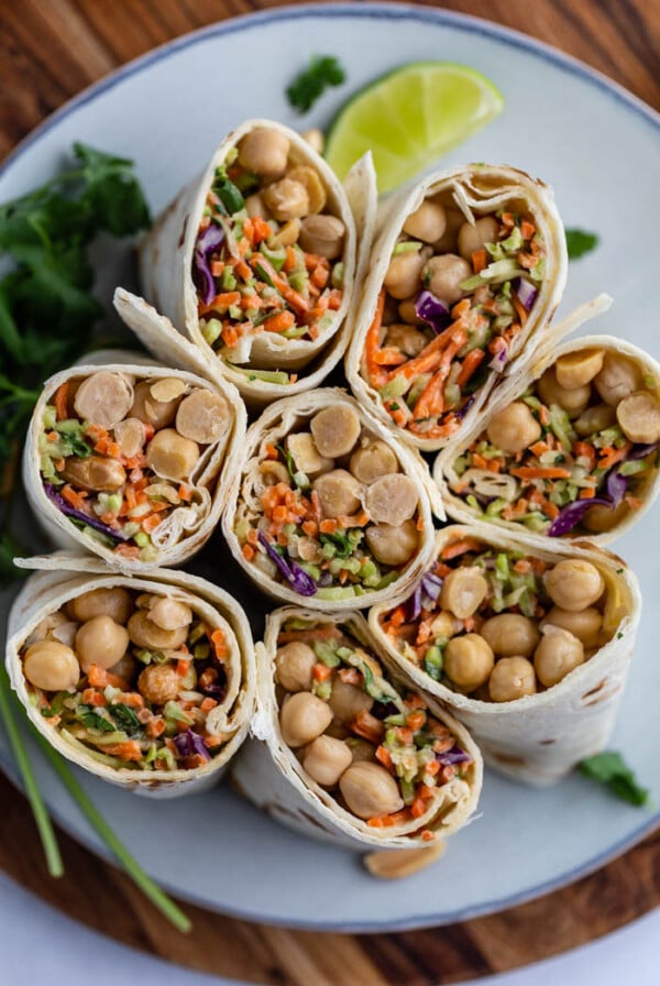 tortilla wraps filled with coleslaw mix and chickpeas. the wraps are cut in half and standing up on a plate so that you can see everything inside of them