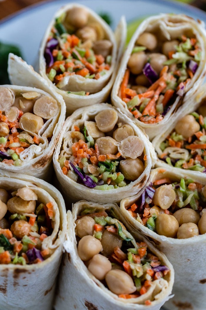 tortilla wraps filled with coleslaw mix and chickpeas. the wraps are cut in half and standing up on a plate so that you can see everything inside of them