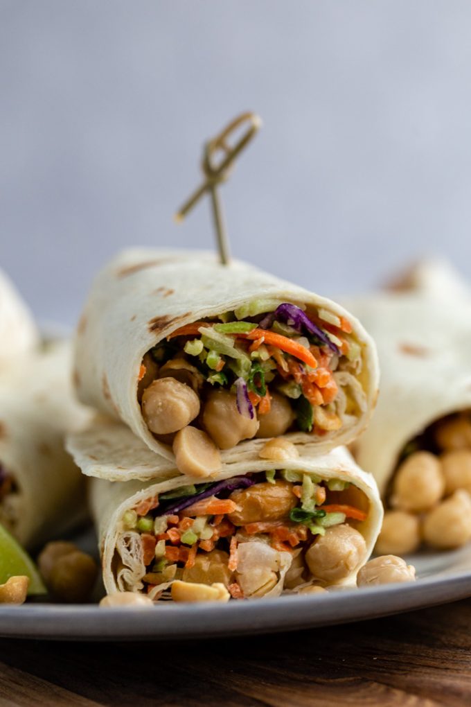 chickpea tortillas wraps filled with veggie slaw and whole chickpeas. The wrap is cut in half and stacked on top of itself so you can see the inside. with a toothpick in the top to hold it together