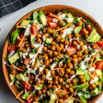 Large salad in a wood bowl with lettuce and chopped veggies topped with roasted chickpeas and drizzled with vegan ranch dressing