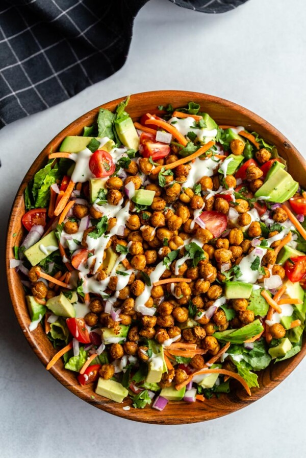 Large salad in a wood bowl with lettuce and chopped veggies topped with roasted chickpeas and drizzled with vegan ranch dressing
