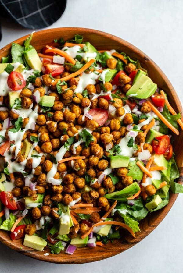 Large salad in a wood bowl with lettuce and chopped veggies topped with roasted chickpeas and drizzled with vegan ranch dressing