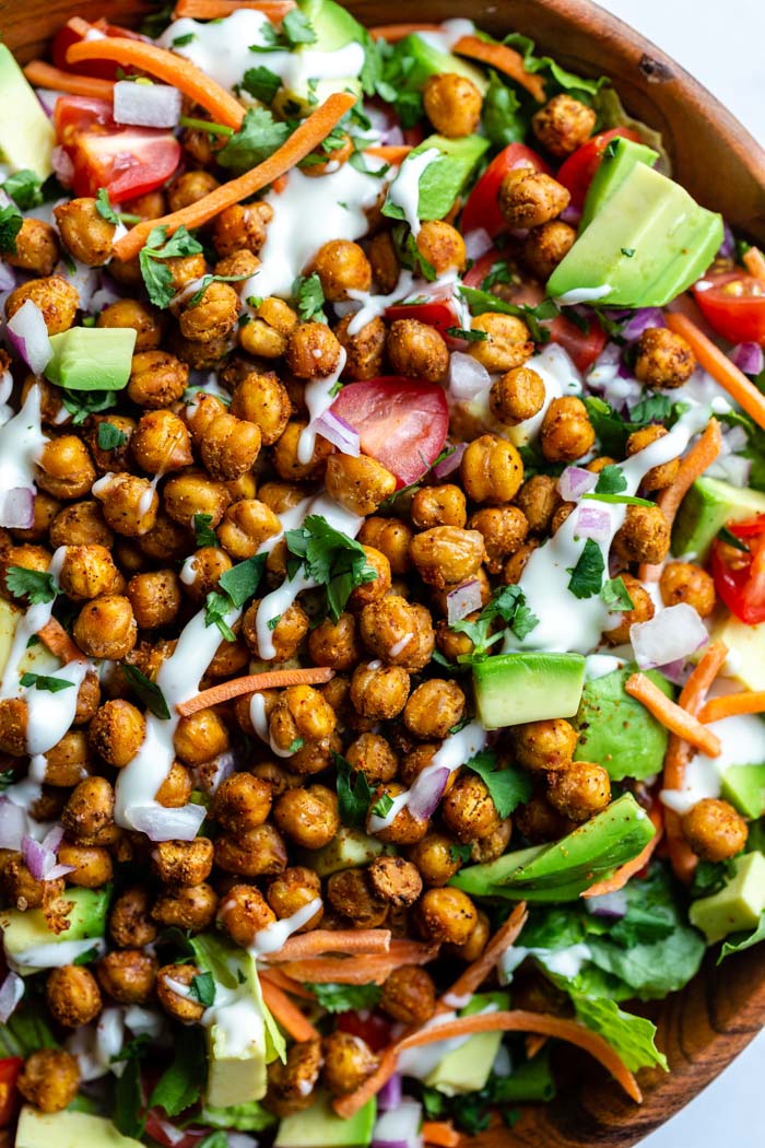 up close shot of Large salad in a wood bowl with lettuce and chopped veggies topped with roasted chickpeas and drizzled with vegan ranch dressing