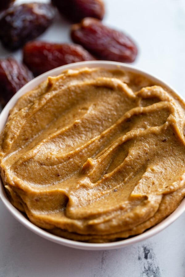 creamy date paste in a small bowl with fresh dates around the bowl