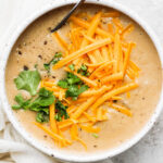 Crockpot potato soup served in a white bowl with cheddar cheese.