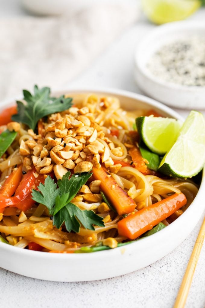 vegan Pad Thai served in a white bowl with chopped peanuts and lime wedges