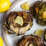 4 artichoke halves on a large plate. 1 is cut side down and the others are cut side up and all crispy with slices of lemon in the middle