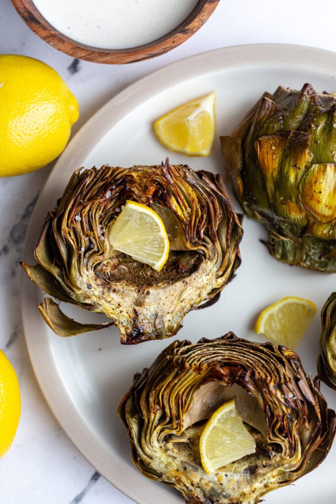 4 artichoke halves on a large plate. 1 is cut side down and the others are cut side up and all crispy with slices of lemon in the middle