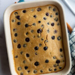 baked oats with blueberries in a small casserole dish with a napkin and spoons on the side