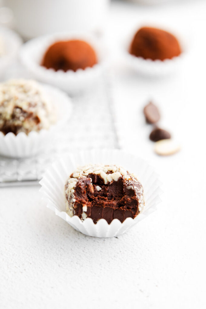 chocolate truffles covered in nuts and sitting in a mini muffin liner with more truffles around