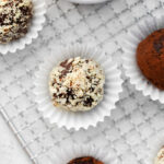 chocolate truffles covered in nuts and sitting in a mini muffin liner with more truffles around