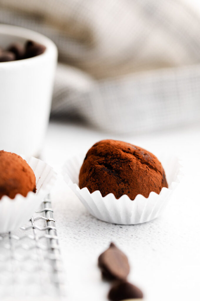 chocolate truffle dusted with cocoa powder and sitting into a small cupcake liner. more truffles in the background