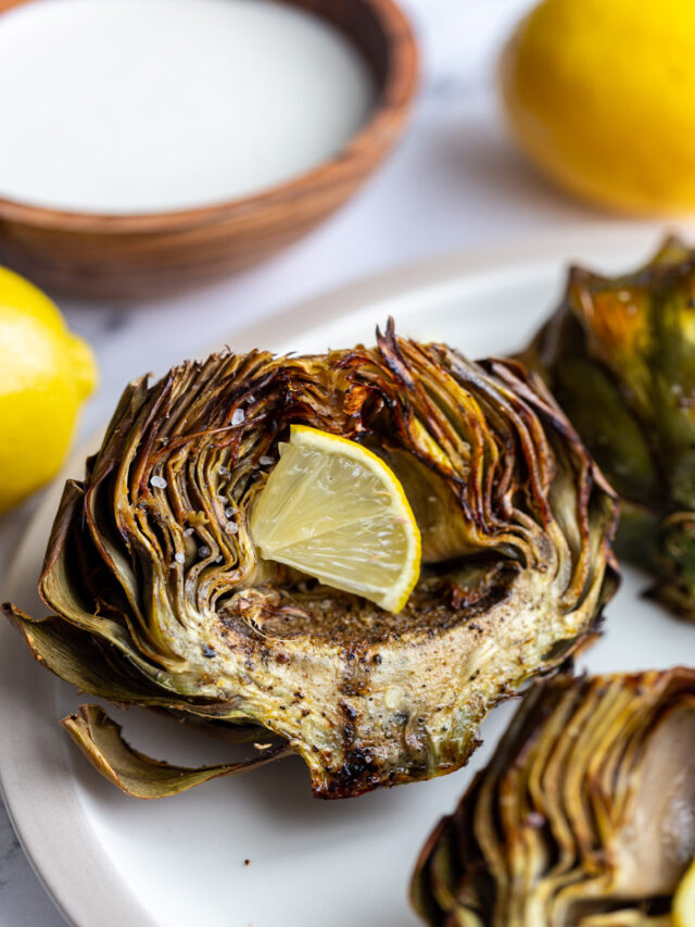 cooked artichoke on a plate with a lemon wedge