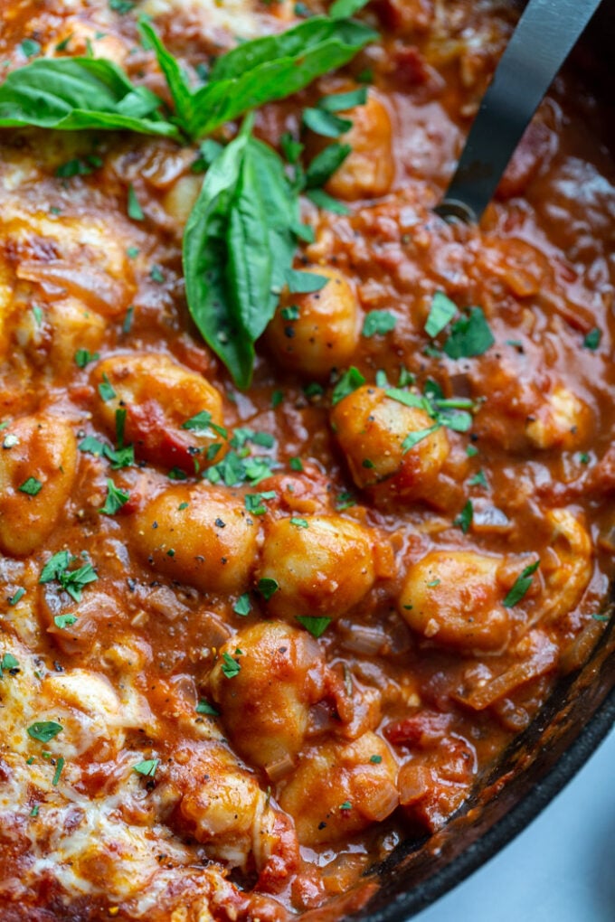 skillet with tomato sauce and gnocchi covered with cheese and garnished with fresh basil. spoon sticking out the side