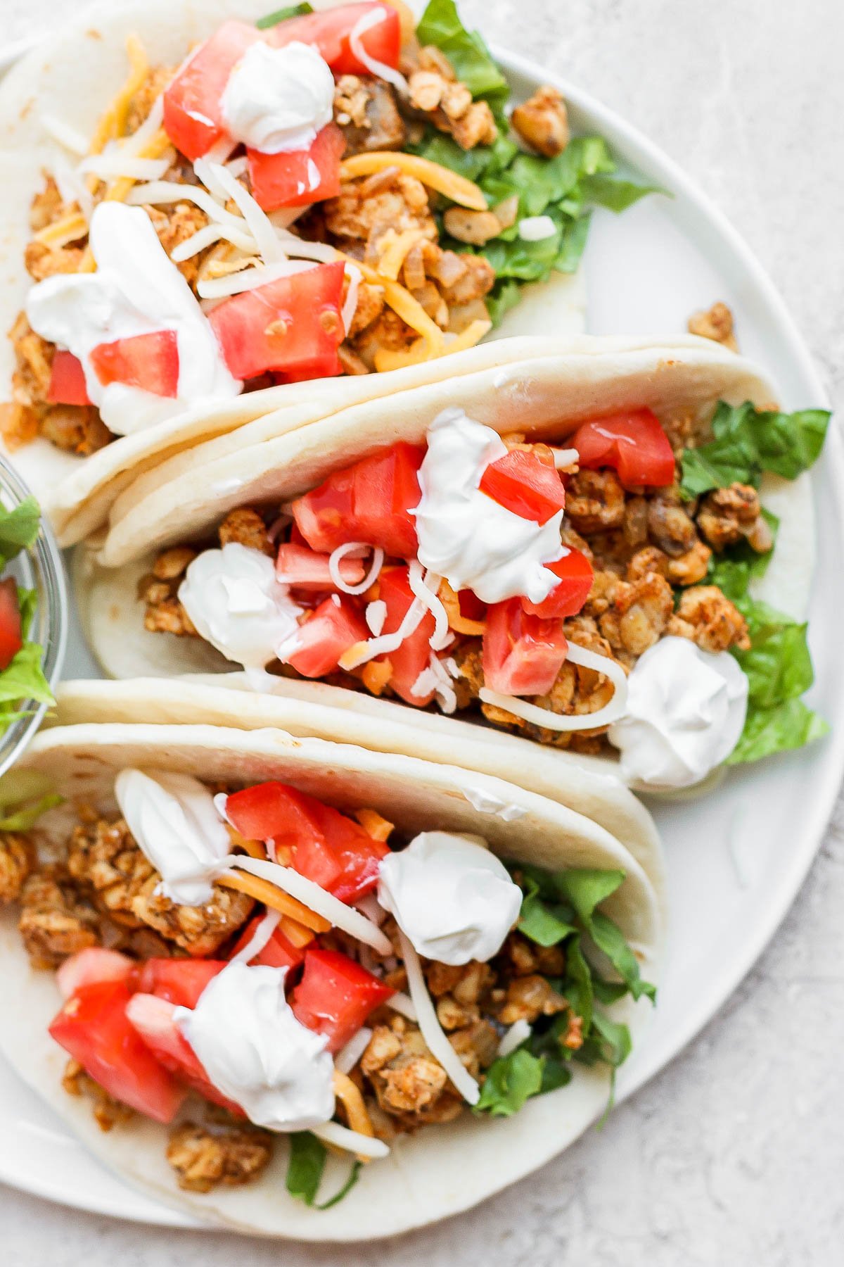 tempeh tacos on a flour tortilla with cheese and fresh veggies on top
