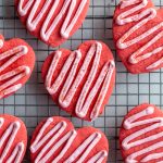 red heart cookies on a cooling rack topped with a light pink zig zag frosting
